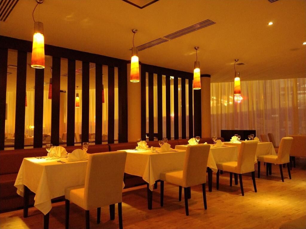 Un restaurant dont les tables sont dressées pour le service, avec un intérieur chaleureux et des luminaires verticaux.