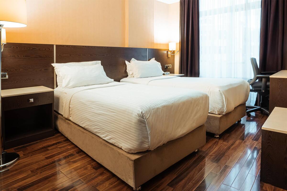A hotel room with two beds, wooden flooring, a desk, and a chair.