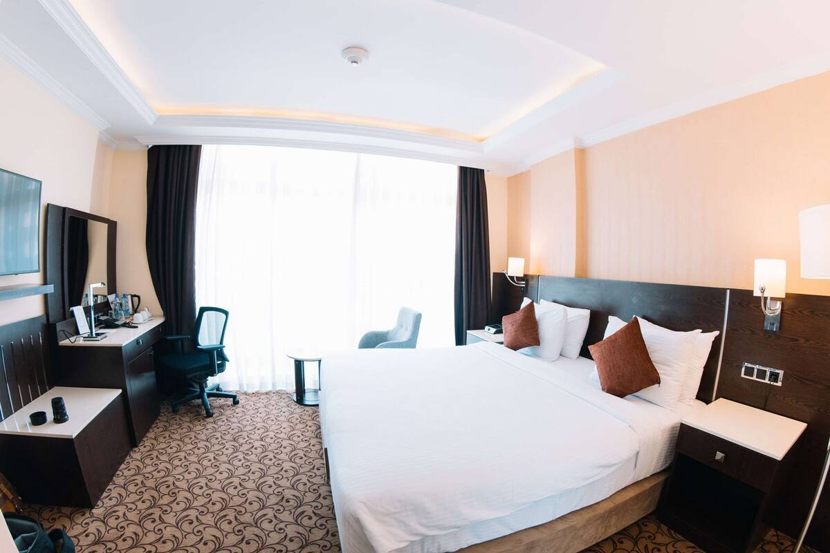 A hotel room with a large bed, a desk with a chair, a TV, and a window with curtains.