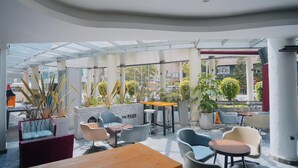 Een terras met moderne zitplaatsen, waaronder stoelen en tafels, omgeven door plantenbakken en een glazen dak.