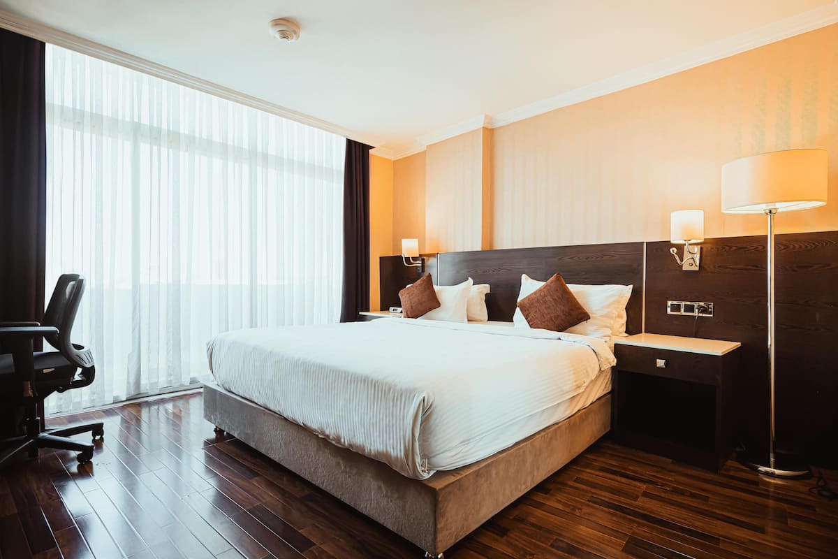 A hotel room with a large bed, a desk, a chair, and a lamp.
