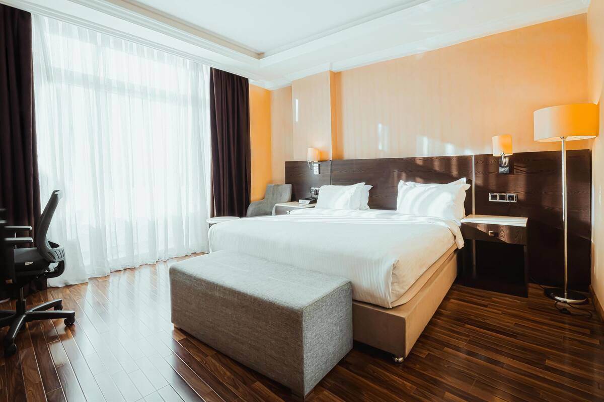 A hotel room with a large bed, a desk, a chair, and a lamp.
