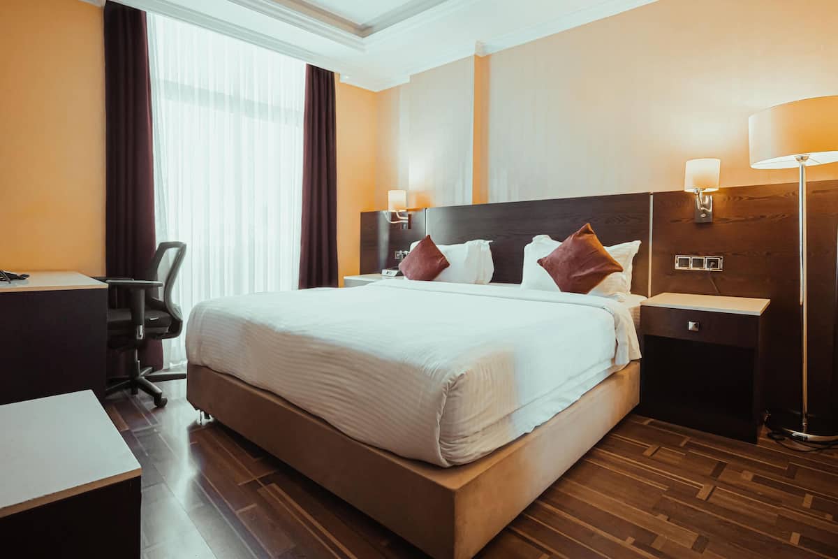 A hotel room with a large bed, a desk, a chair, and two bedside lamps.
