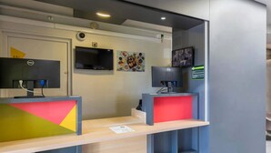 A reception desk with two computer stations, a flat-screen TV, and a wall-mounted artwork. - B&B HOTEL Bourges (1) (Bourges)