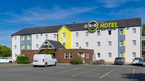 A B&B hotel with a yellow and white facade, a parking lot, and a white van parked in front. - B&B HOTEL Bourges (1) (Bourges)
