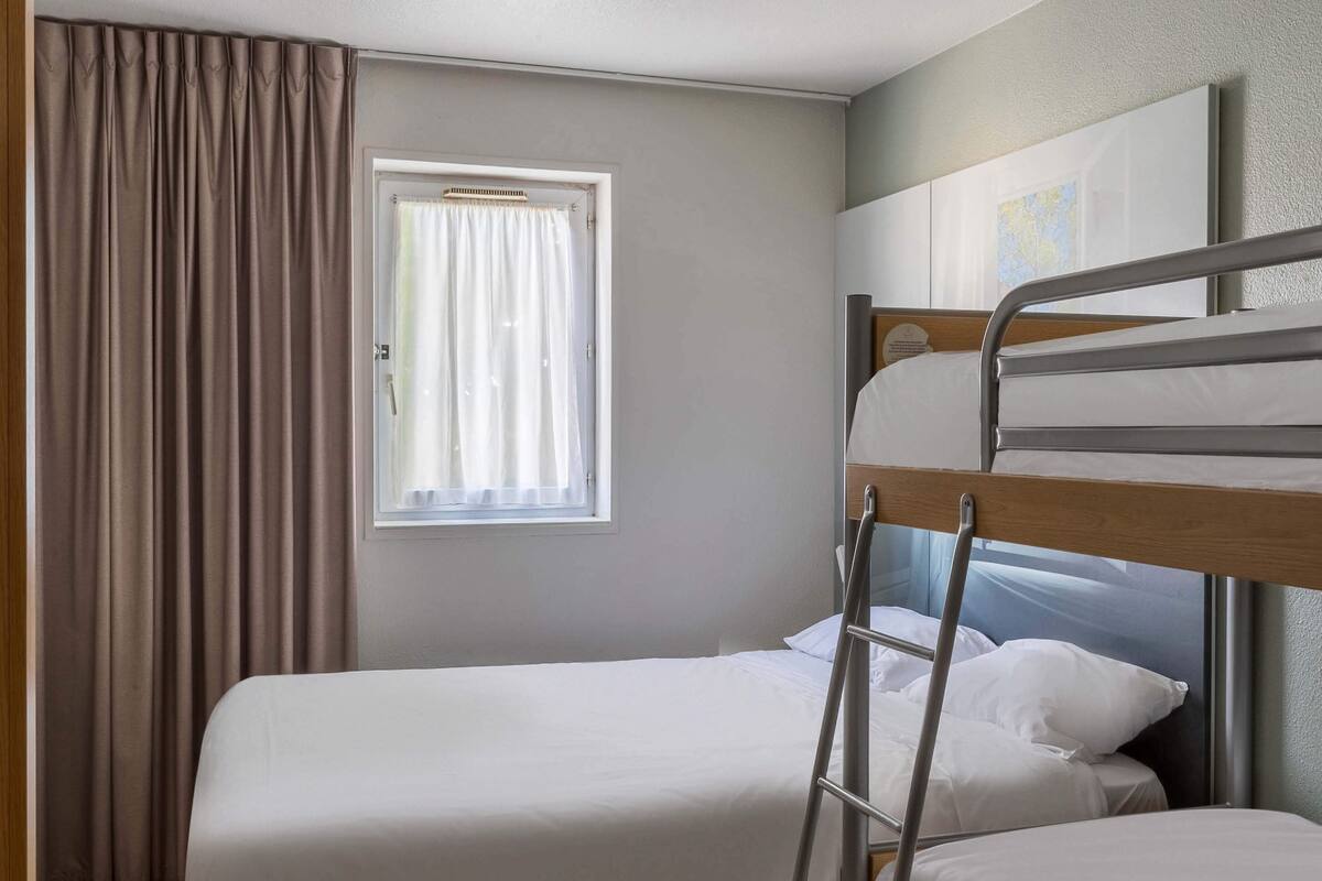 A single bed with a metal ladder, a window with curtains, and a map on the wall.