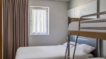 A single bed with a metal ladder, a window with curtains, and a map on the wall.