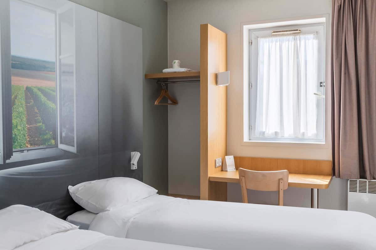 A hotel room with a bed, a desk, and a window with curtains.