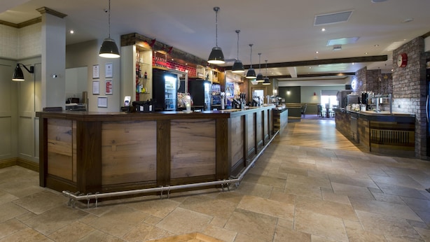 A bar area with a wooden counter, pendant lighting, and a tiled floor. - Premier Inn Abergavenny (Llanfoist)