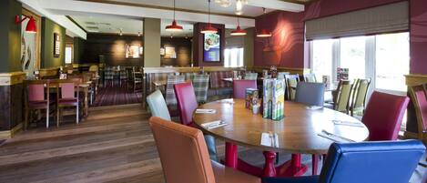 A restaurant with a wooden floor, round tables, and colorful chairs.