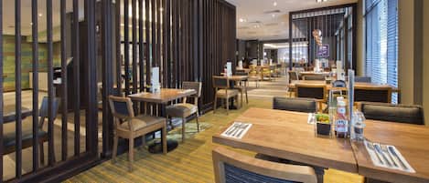 A modern hotel dining area with wooden tables, chairs, and a striped carpet.