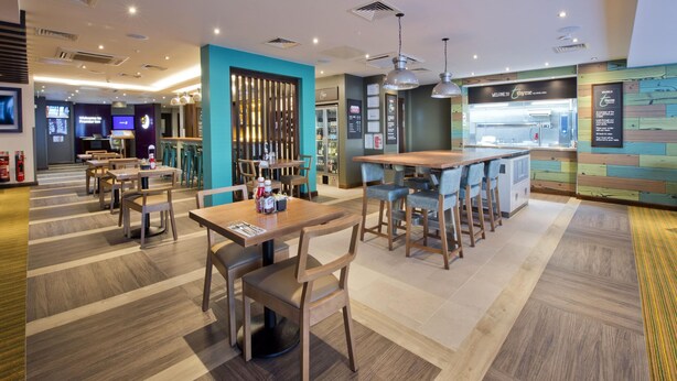 Un restaurant moderne avec des tables et des chaises en bois, un bar et une cuisine visible au fond de la salle.