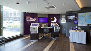 Zona reception di un hotel con una scrivania per il check-in, uno schermo televisivo, una mappa del mondo e un cartello con la 'Good Night Guarantee'.