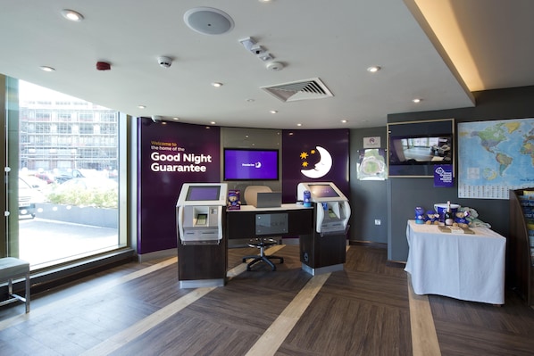 A hotel reception area with a check-in desk, a television screen, a world map, and a 'Good Night Guarantee' sign. - Premier Inn London Woolwich Royal Arsenal (London)