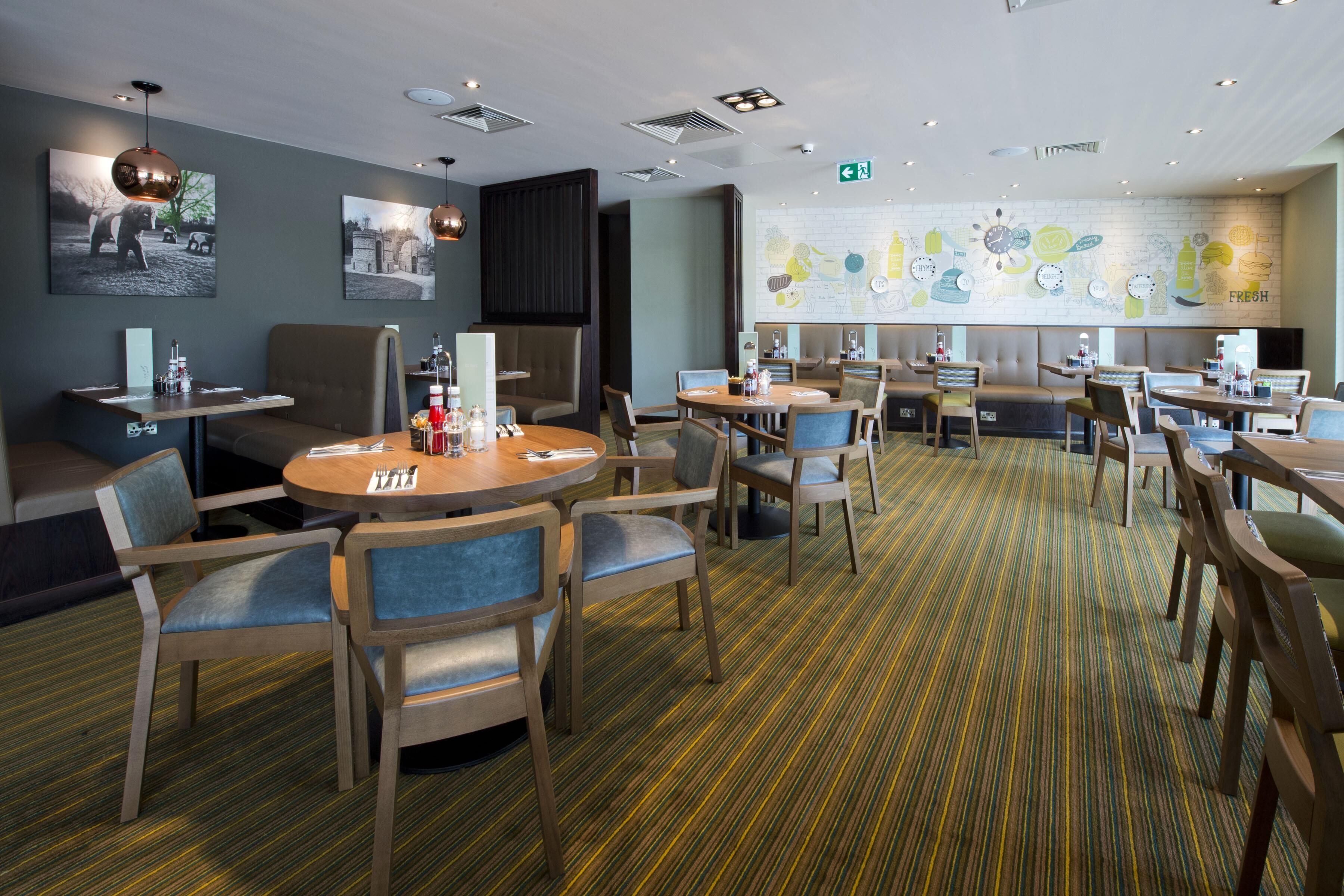 A hotel dining area with round tables, cushioned seating, and a patterned carpet.