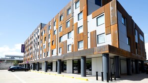 A modern multi-story hotel with a flat roof, large windows, and a parking area with yellow curbs. - Premier Inn Milton Keynes Central - Theatre District (Milton Keynes)