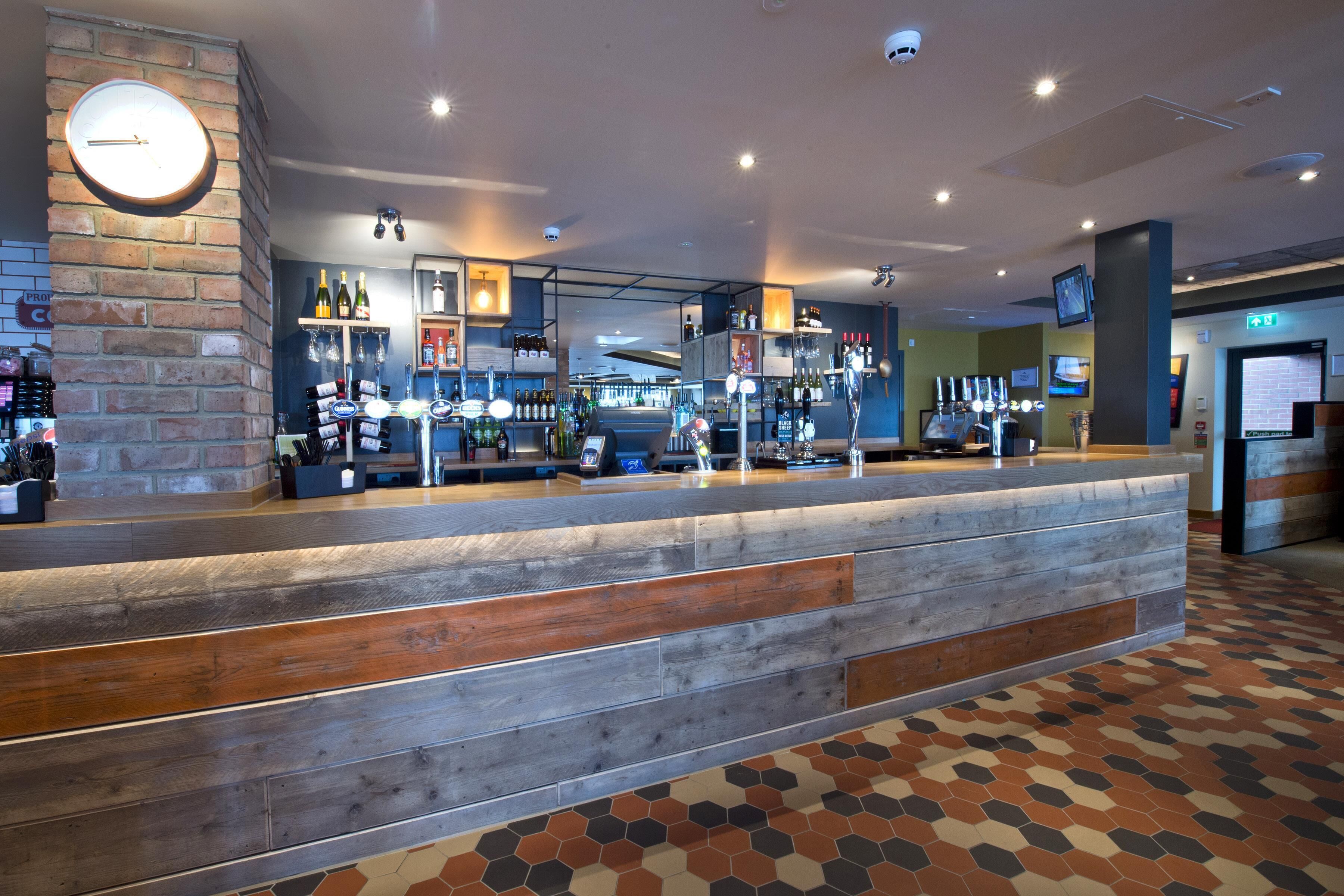 Un espace bar avec un comptoir en bois, des étagères remplies de bouteilles et une horloge au mur.