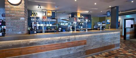 Un espace bar avec un comptoir en bois, des étagères remplies de bouteilles et une horloge au mur.