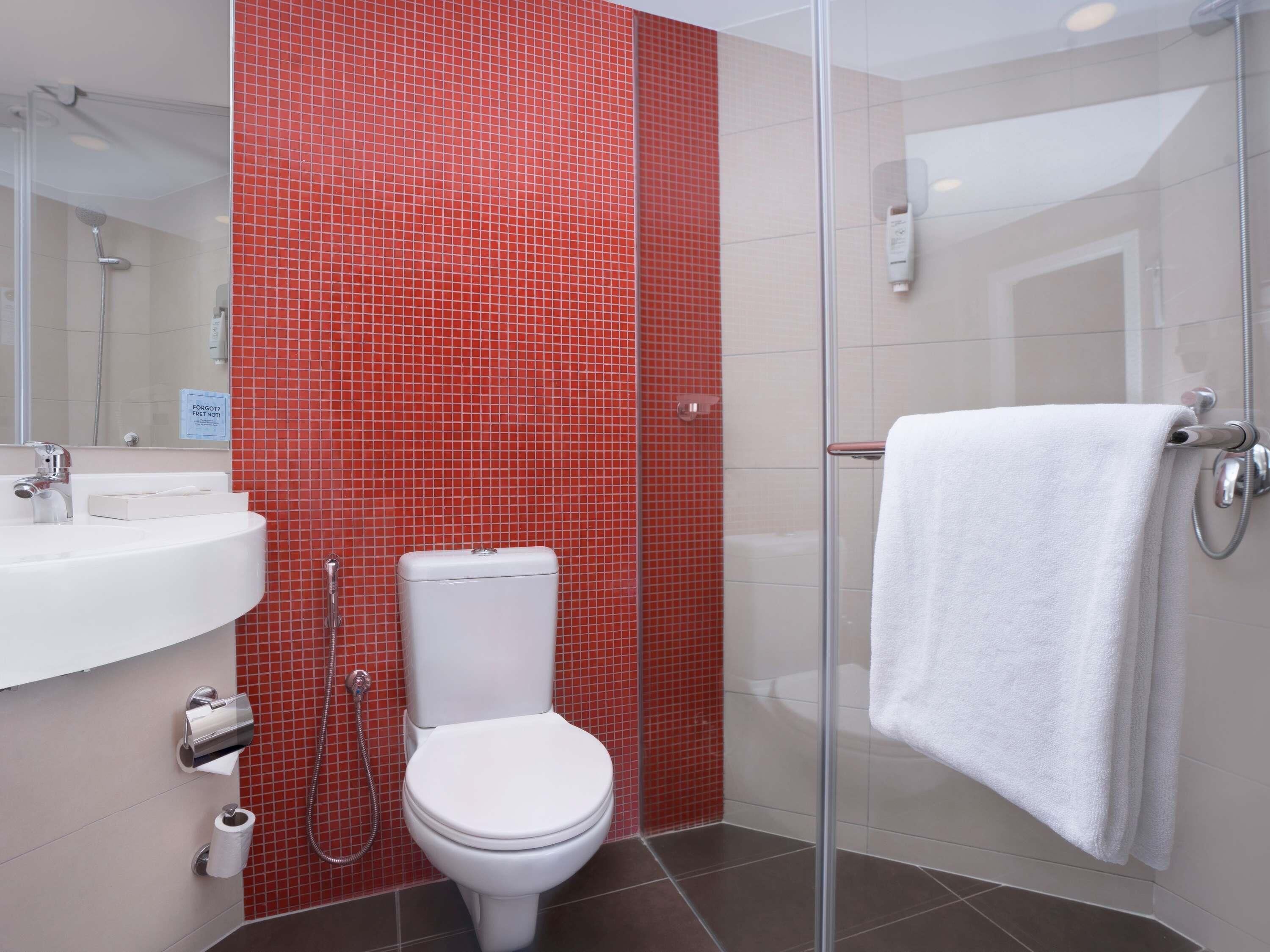 Een badkamer met een wit toilet, een wastafel, een glazen douchecabine en een handdoek aan de douchedeur.