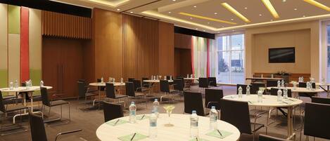 A conference room with round tables, chairs, water bottles, and a television screen.
