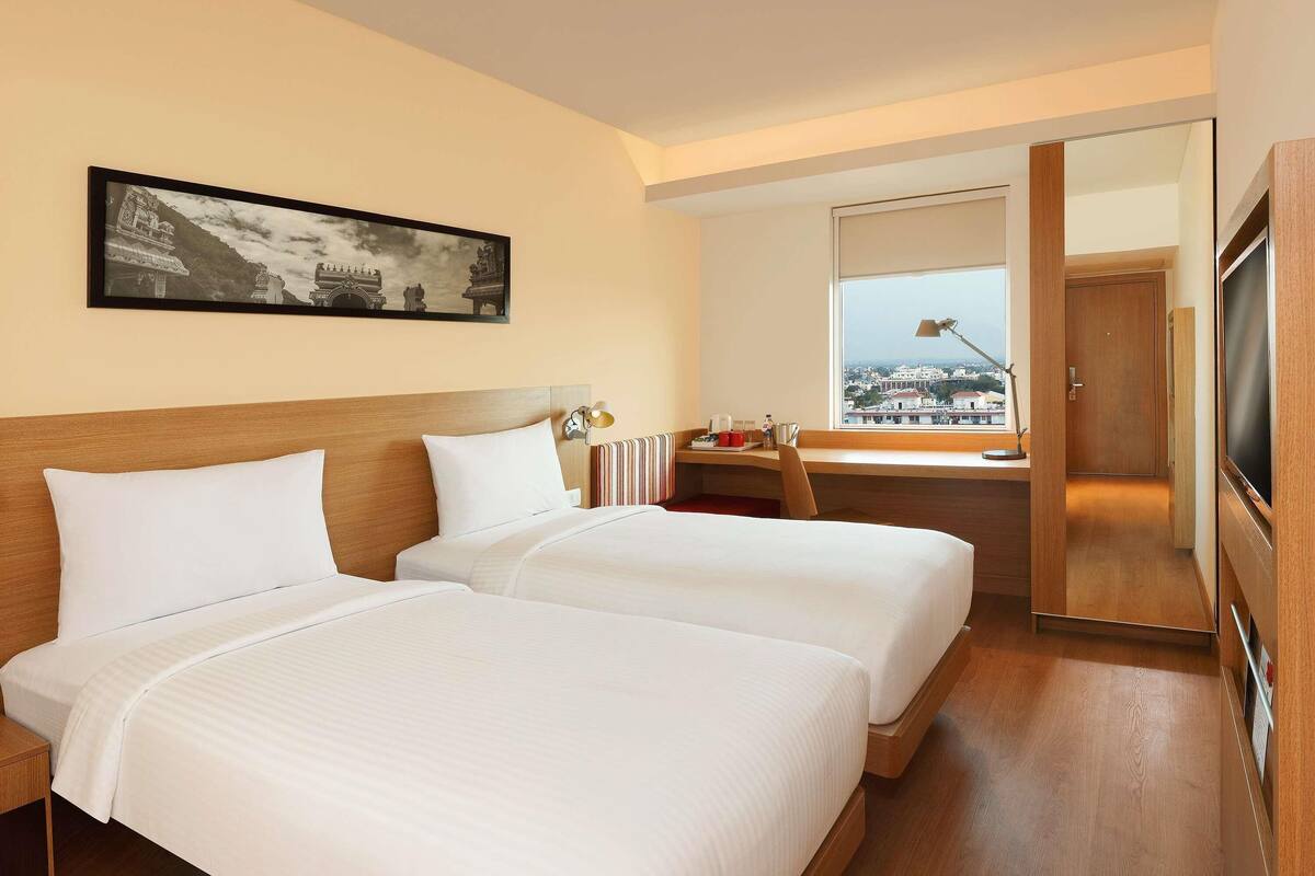 Een hotelkamer met twee bedden, een bureau met lamp, een televisie en een ingelijste foto aan de muur.