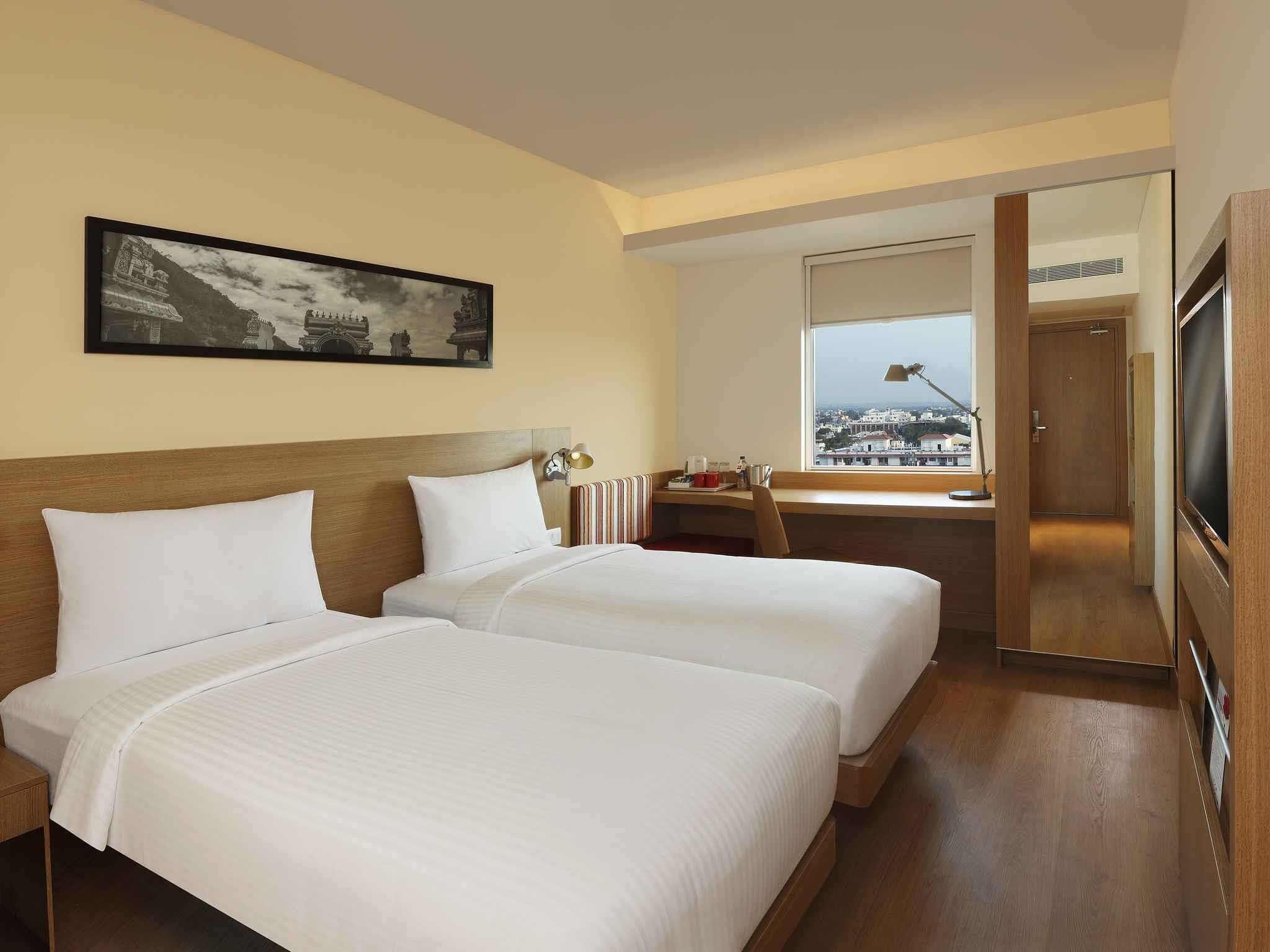 A hotel room with two beds, a desk, a chair, a TV, and a window with a city view.