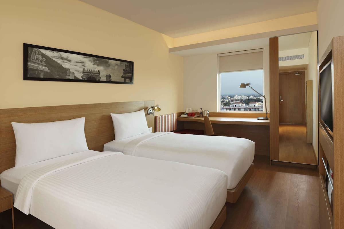 A hotel room with two beds, a desk, a chair, a TV, and a window with a city view.