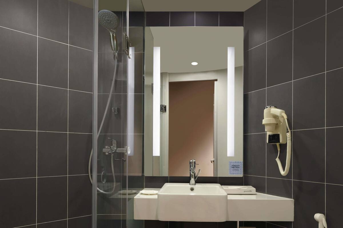 Een moderne badkamer met een douchecabine van glas, een wastafel met twee kommen en een haardroger bevestigd aan de muur.