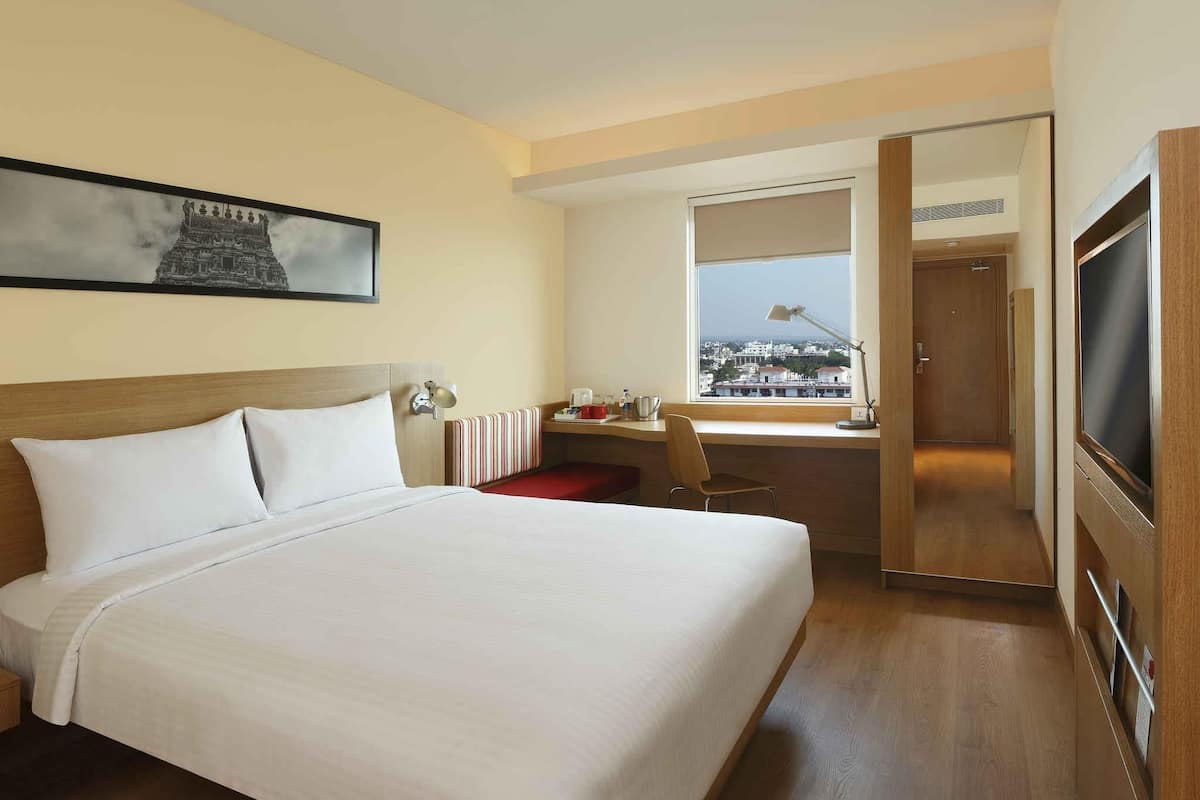 Hotelkamer met een groot bed, een bureau met stoel, een televisie en een raam met uitzicht over de stad.