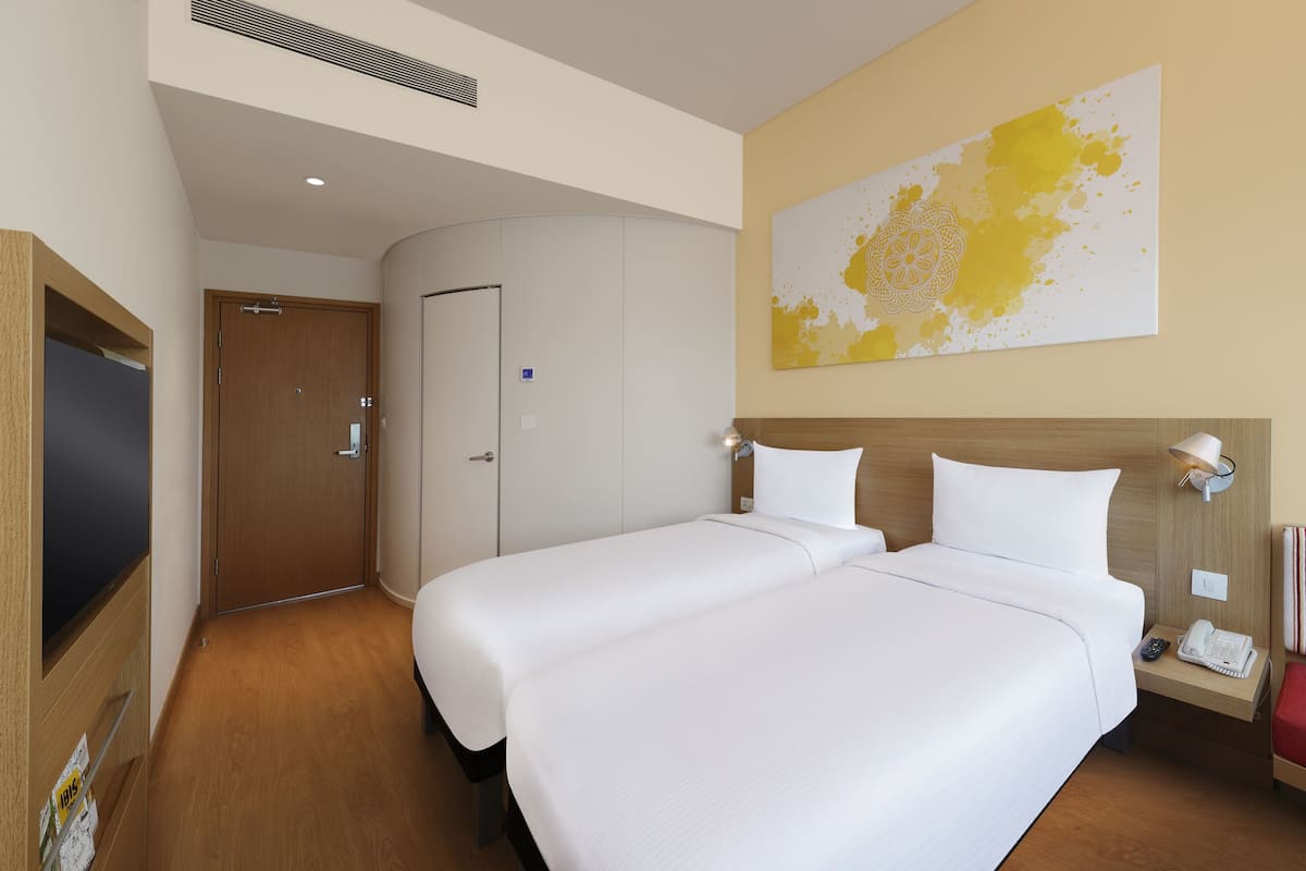 Een hotelkamer met twee bedden, een houten hoofdbord, een rode gestreepte bank, een aan de muur bevestigd telefoon en een groot abstract schilderij.