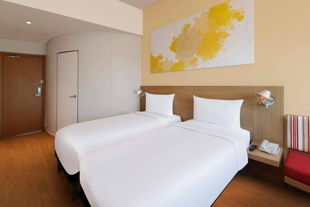 Hotelkamer met twee bedden, een houten hoofdbord, een nachtkastje met een lamp, een telefoon en een gestreept kussen.