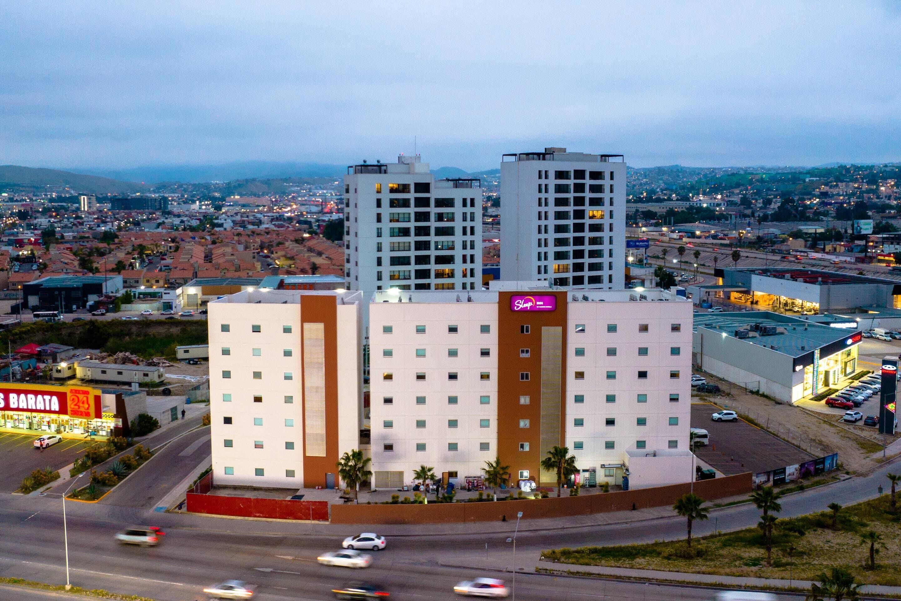 A multi-story hotel with a central atrium, surrounded by a parking area and a busy road.