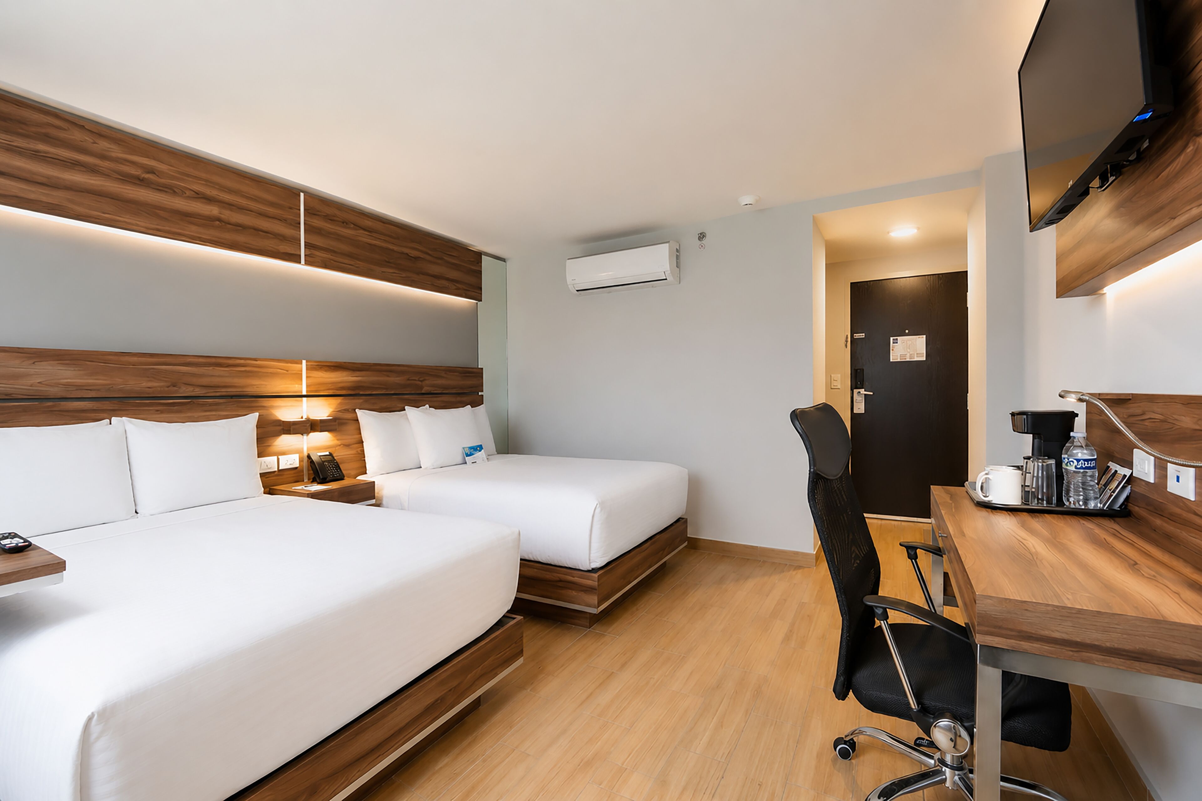Een hotelkamer met twee bedden, een bureau met een stoel, een flatscreen-televisie en een airconditioning.