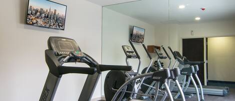 A gym with treadmills, a mirrored wall, and a cityscape painting.