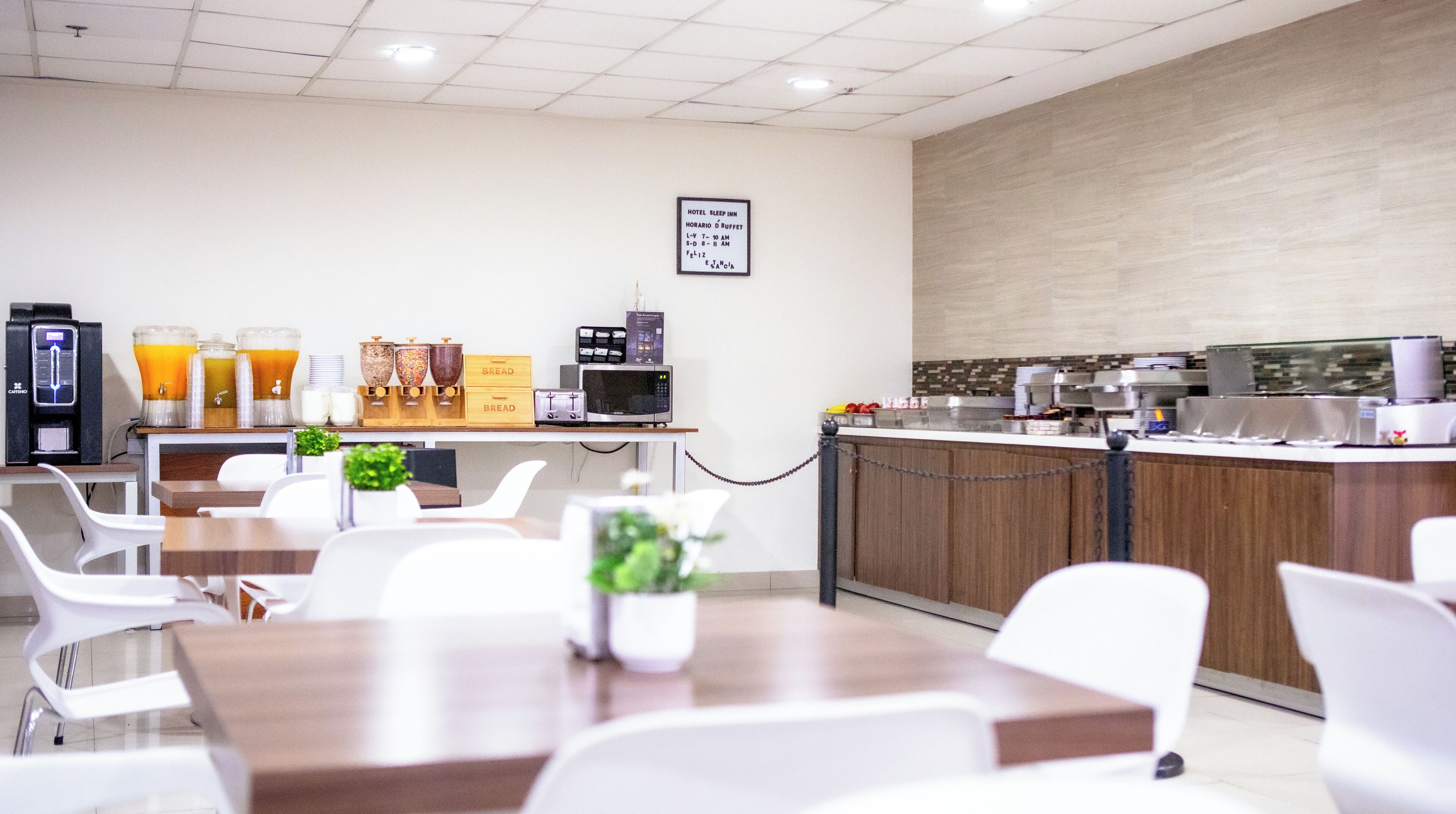 Ein Frühstücksbereich eines Hotels mit Tischen, Stühlen, einer Kaffeemaschine und einem Buffet.