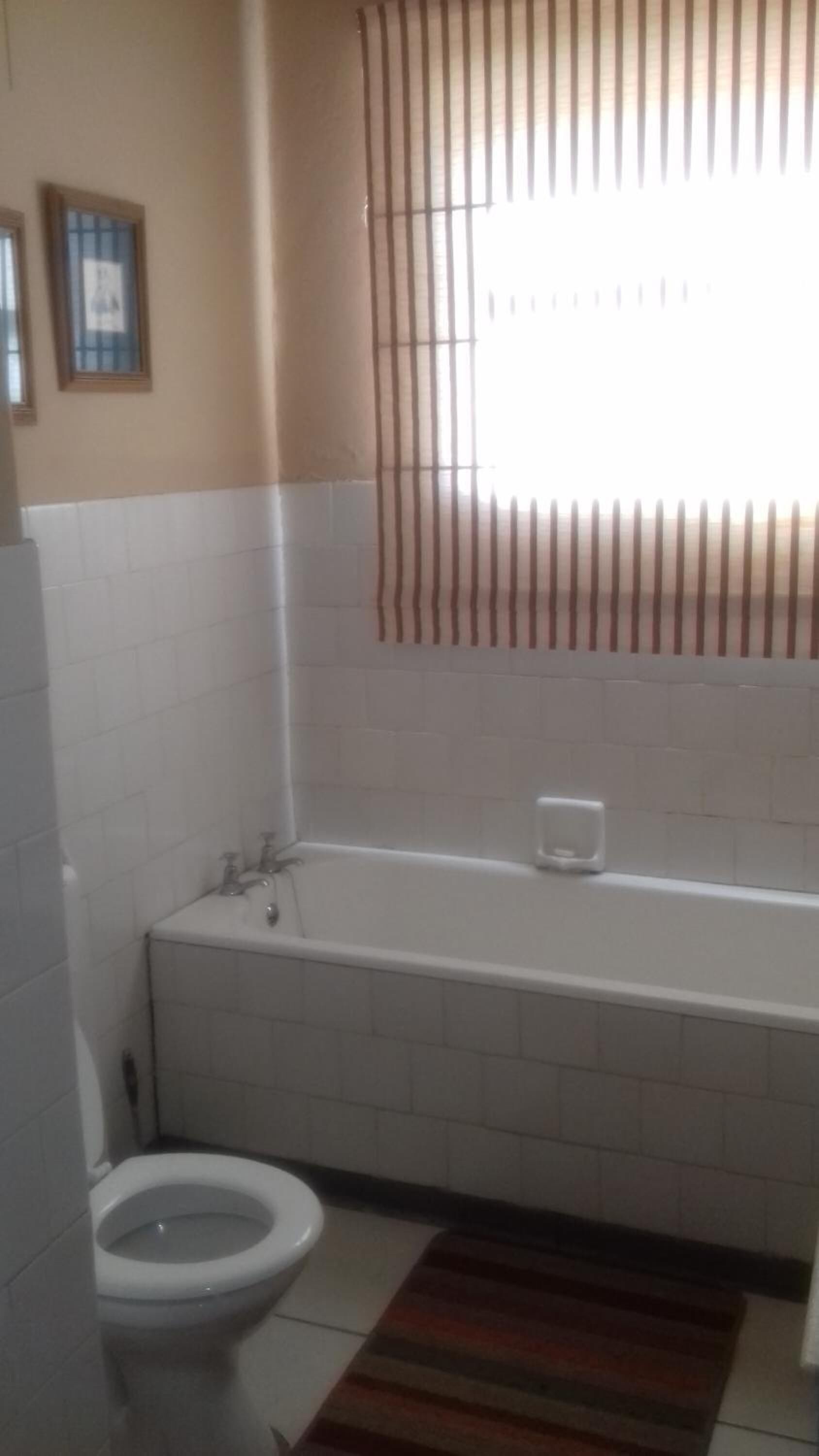 A bathroom with a toilet, a bathtub, and a window with vertical blinds.