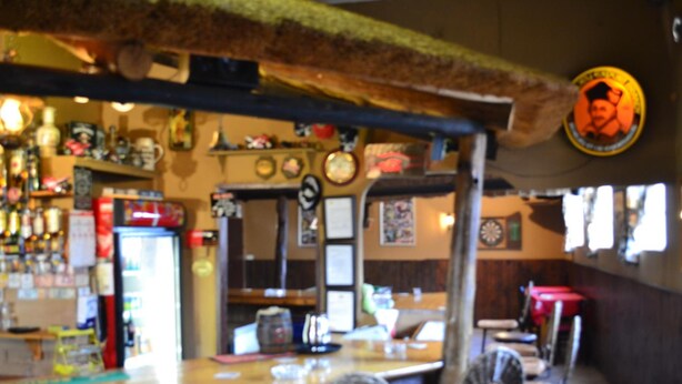 Eine Bar mit Theke, Stühlen und verschiedenen Gegenständen auf Regalen.