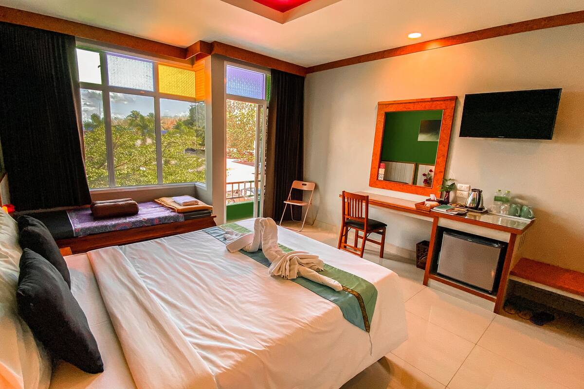 Hotelkamer met een groot bed, een bureau met stoel, een televisie en uitzicht op groen.