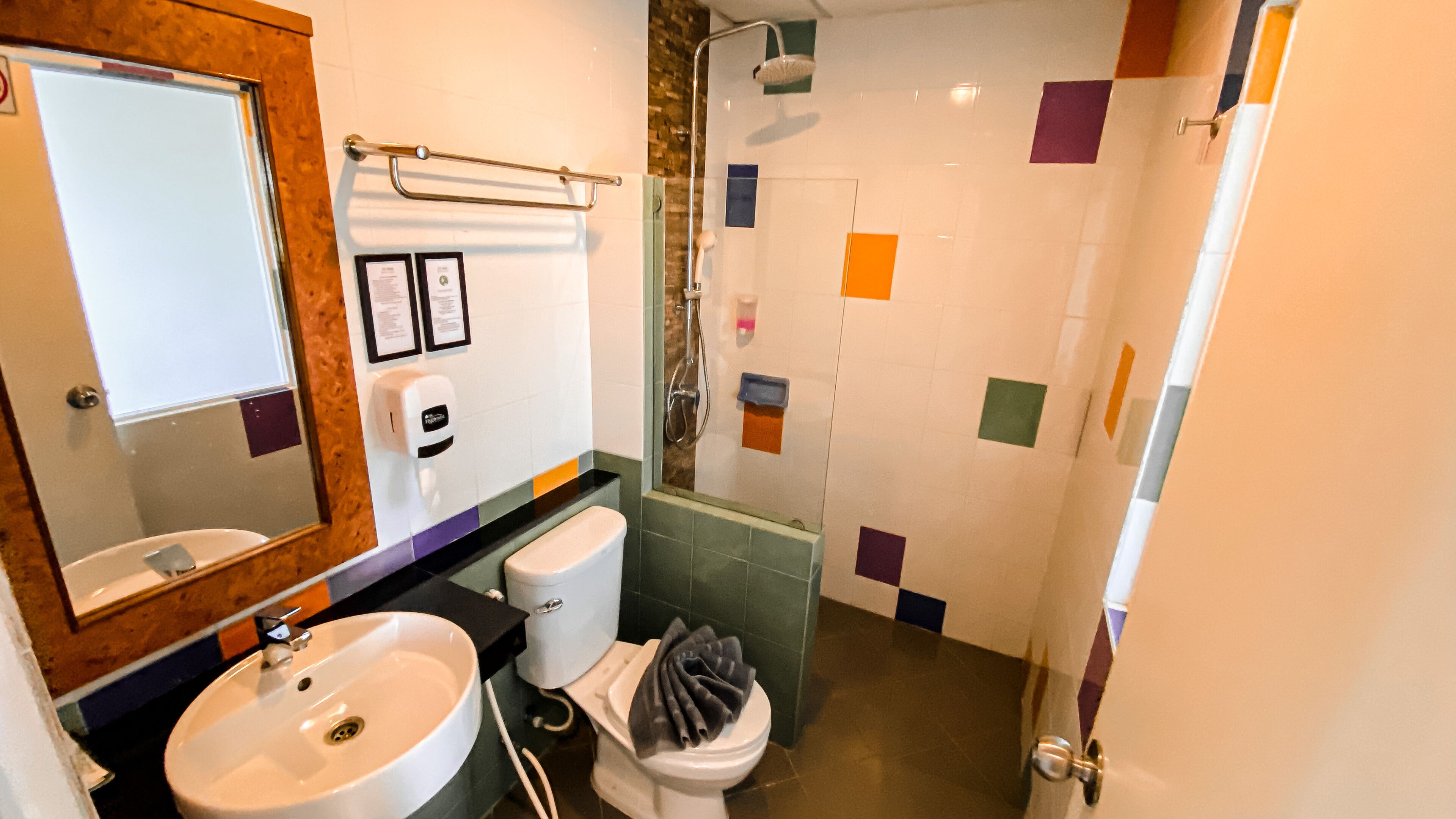 Une salle de bain avec un lavabo, des toilettes et une douche. Des certificats encadrés sont accrochés au mur, et une serviette est posée sur les toilettes.