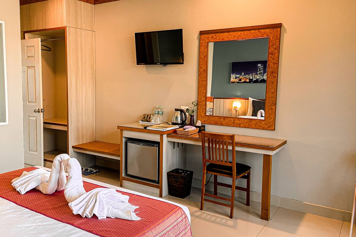 Een hotelkamer met een bed, een bureau met stoel, een spiegel, een televisie en een kledingkast.
