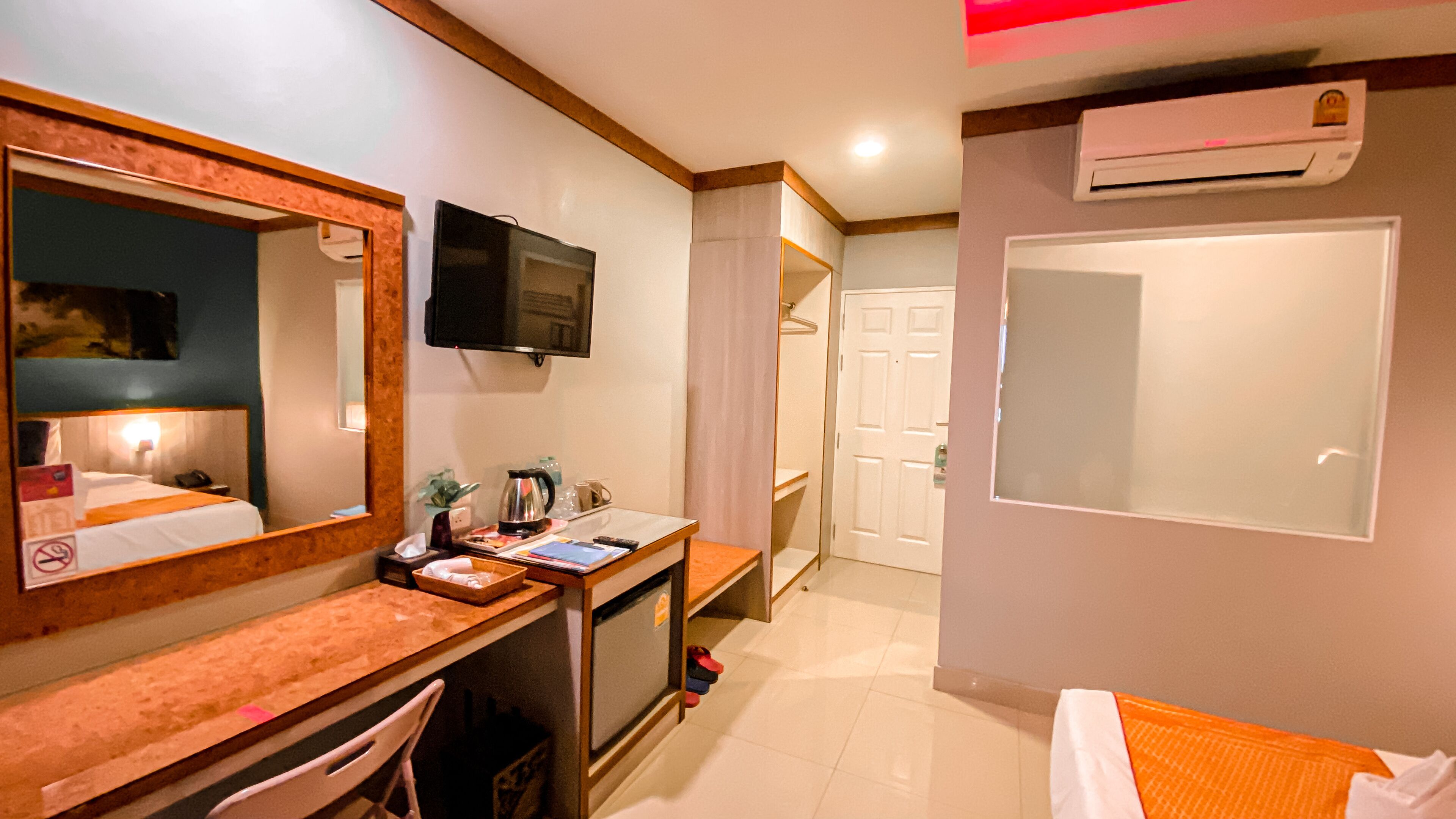 Habitación de hotel con cama, escritorio con computadora, televisor, espejo, ducha y aire acondicionado.