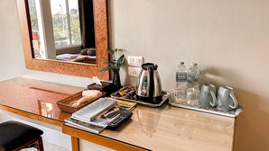 Habitación de hotel con un escritorio de madera, un espejo, una ventana, una tetera, botellas y una taza.