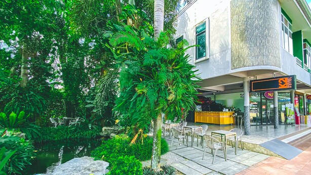 Un hotel con un jardín exuberante, mobiliario exterior y una recepción visible.