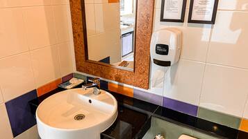 A bathroom with a white sink, a mirror, a soap dispenser, and a towel rack.