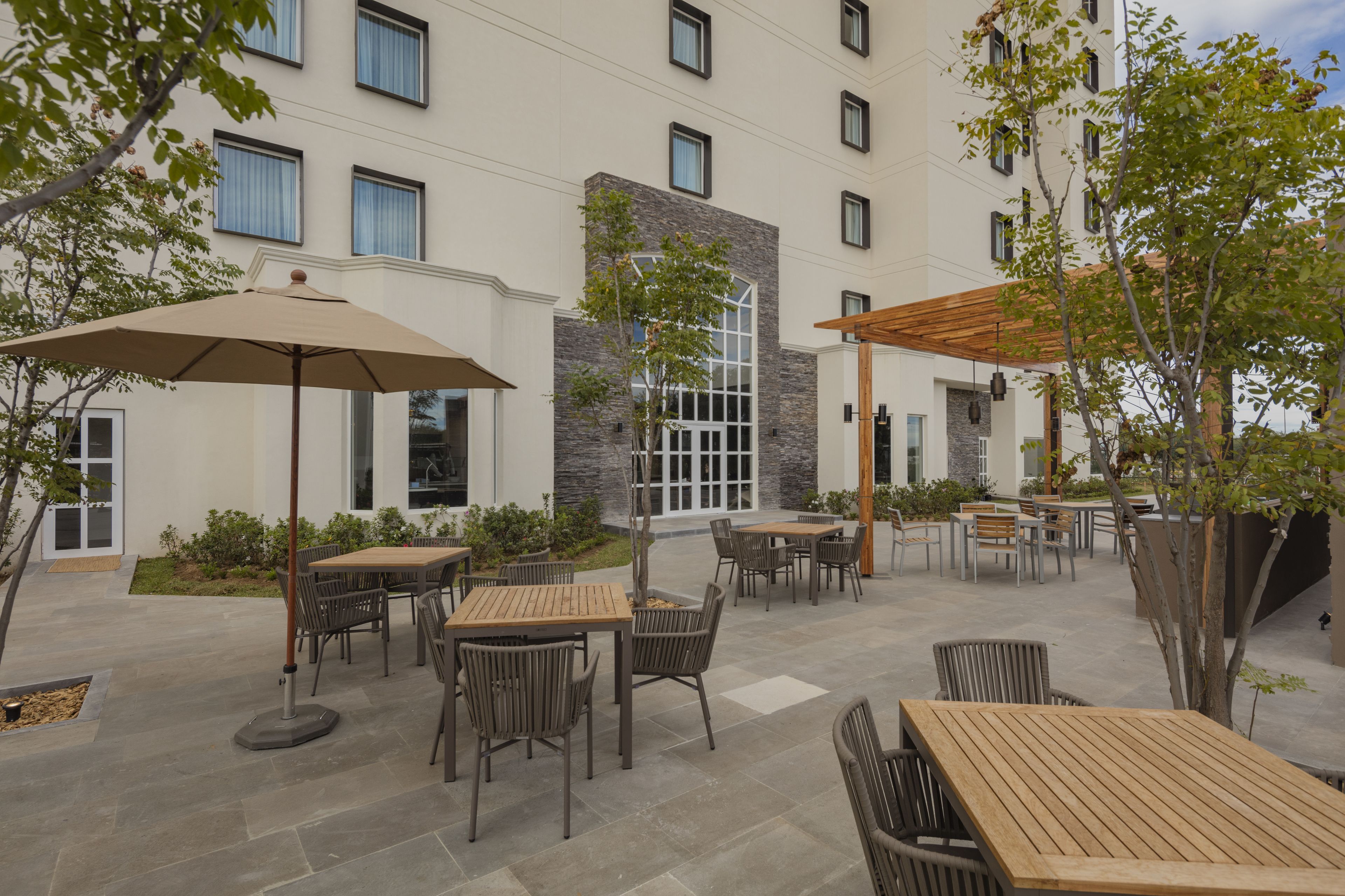 An outdoor patio area with multiple tables and chairs, surrounded by a building with a stone facade and large windows.