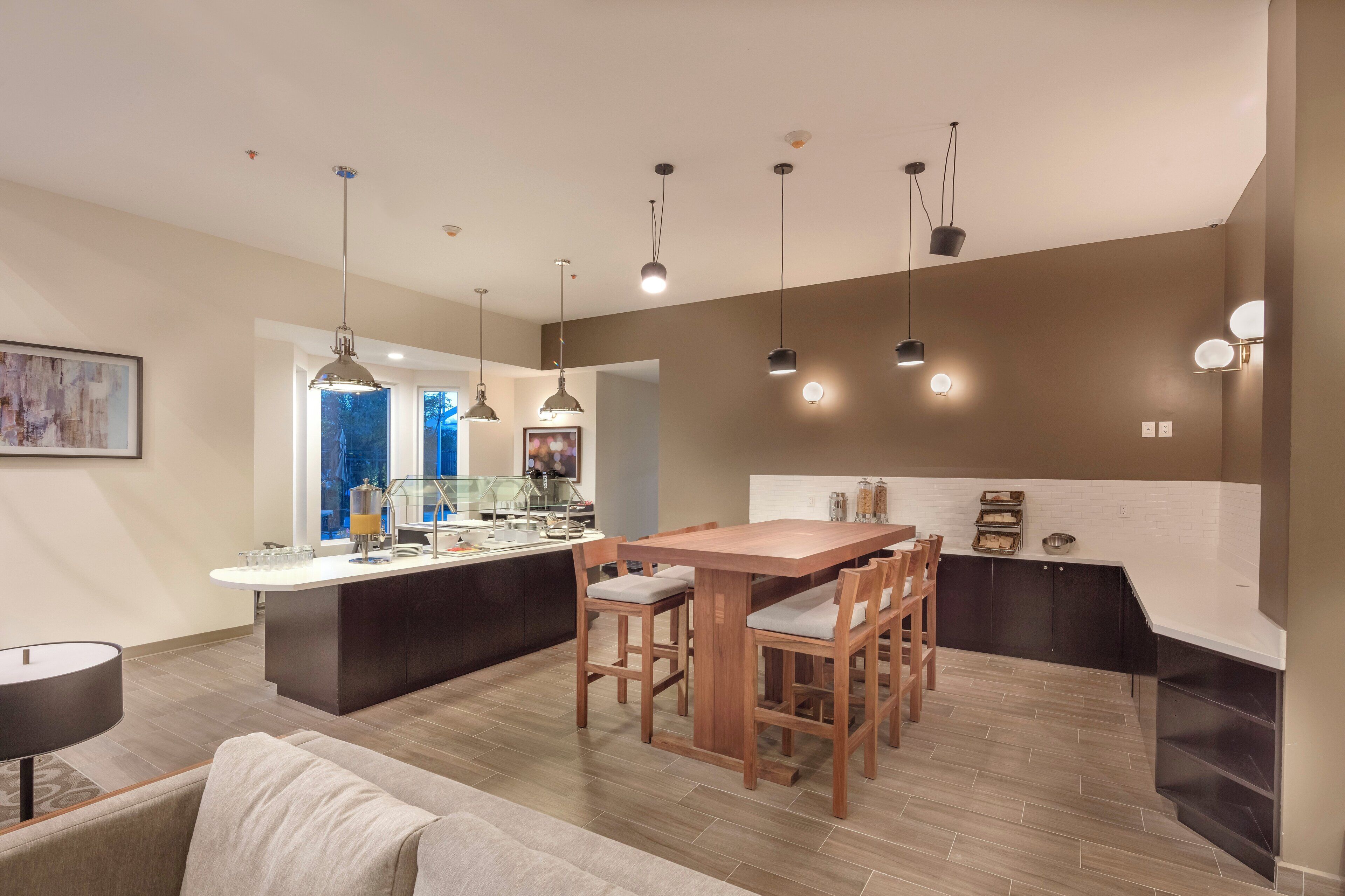 A modern kitchen with a central island, pendant lighting, and a dining area with wooden chairs.