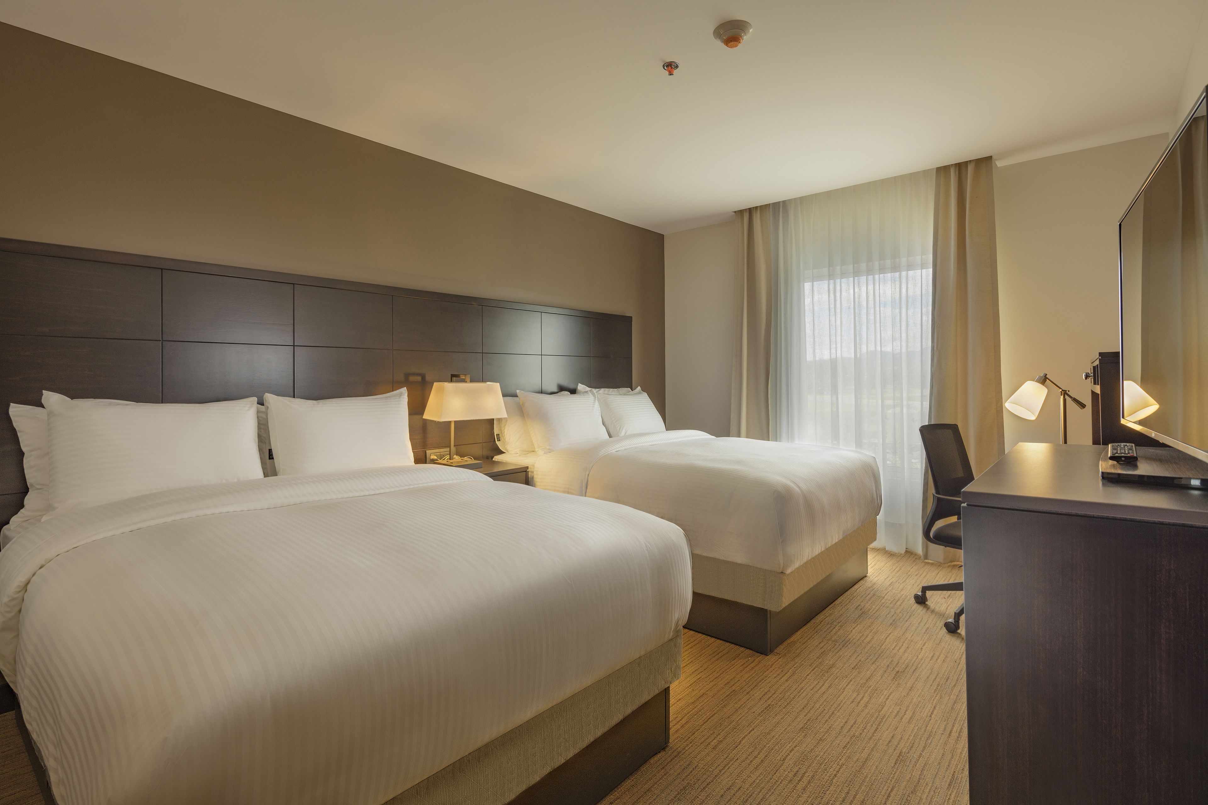 A hotel room with two beds, a desk, a chair, and a large mirror.