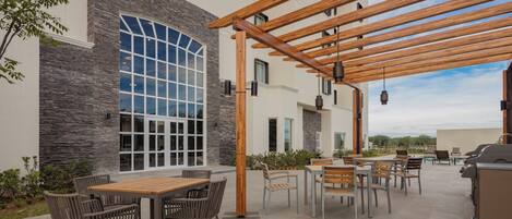 Un espacio al aire libre con patio, una pérgola, mesas, sillas y una estación de barbacoa.