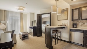 A modern hotel room with a dining area, kitchenette, and a large mirror.