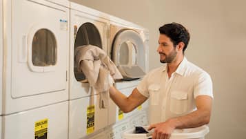 A person in a white shirt loading a laundry basket into a front-loading washing machine.